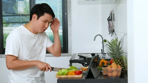 Stressed man cooking and preparing vegetables according to a recipe on a tablet  Stock Footage 170708852