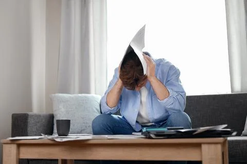 Stressed man on a couch covers his head with unpaid utility bills. Rising i.. Фото