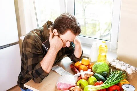 Stressed man with empty wallet and long receipt sits by groceries. Concept .. Foto stock