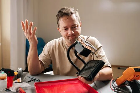 Stressed man holding disassembled computer component, expressing confusion and 库存照片