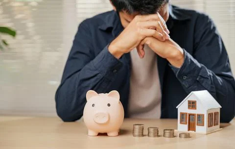 Stressed man holding his forehead, surrounded by a piggy bank, coin stacks,.. Stock Photos