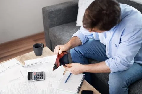 Stressed man looks into an empty wallet surrounded by unpaid utility bills .. Фото