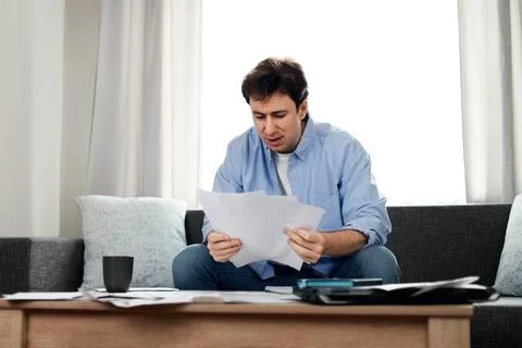 Stressed man reading overdue utility bills at home. He is worried about ris.. Stock Photos
