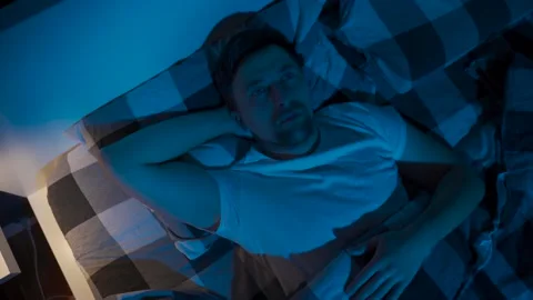 Stressed man trying to sleep in bed at night. Young male with open eyes suffers Stock Footage 145439758