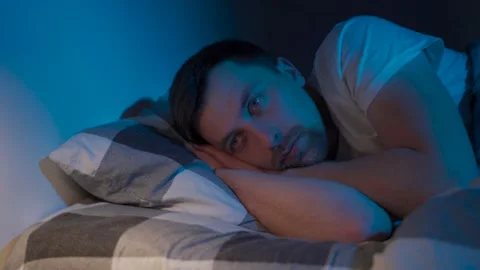 Stressed man trying to sleep in bed at night. Young male with open eyes suffers Stock Footage 145439897
