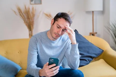 Stressed man using smartphone on sofa at home Stock Photos