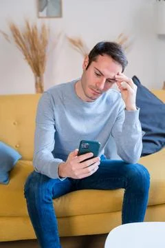 Stressed man using smartphone on sofa at home Stock Photos