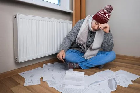 Stressed man in winter hat sitting on floor with calculator and bills near .. Stock Photos