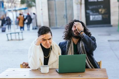 Stressed men looking frustrated while using laptop outdoors at cafe. Stock Photos