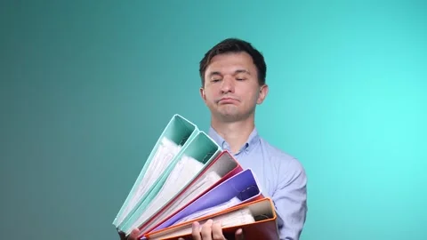 Stressed office worker struggling with a large pile of colorful ring binders Stock Footage 342767940