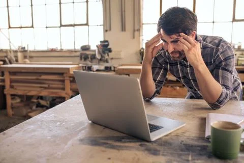 Stressed out woodworker using a laptop in his carpentry studio Stock Photos