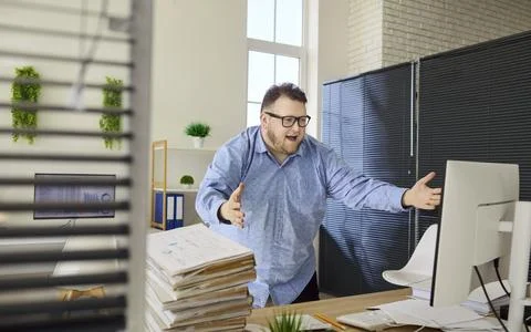 Stressed overweight office worker gesturing at computer with pile of paperwork Foto stock