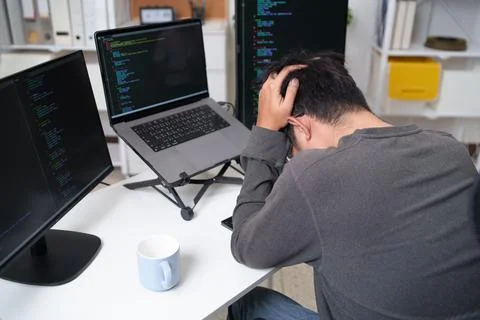 Stressed Programmer Struggling with Code on Multiple Screens in a Tech Stock-Fotos