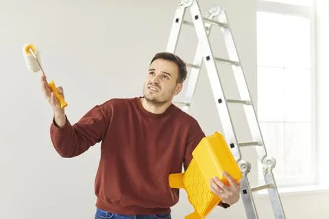 Stressed upset young man painter having problems making repair in empty new Stock Photos