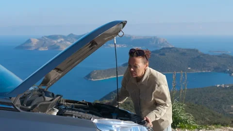 Stressed woman standing by broken down car with open hood Stock Footage 332644415