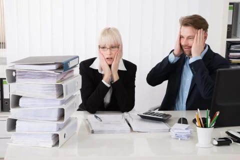 Stressed Young Businesspeople Looking At Stack Of Folders In Office Foto stock