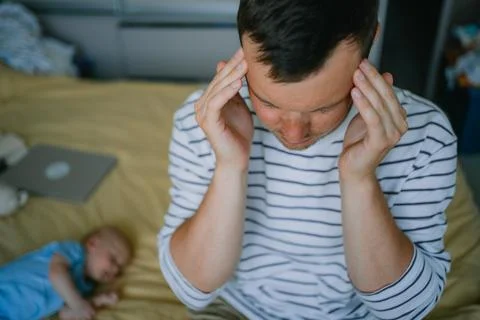 Stressed young father experiencing severe headache due to fatherhood burnout Stock Photos