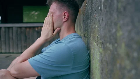 Stressed Young Man Covering Face in Despair Leaning Against Stone Wall Outdoors Stock Footage 339033548