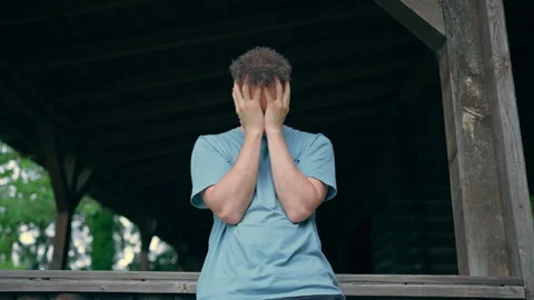 Stressed Young Man Holding Face in Hands Under Shelter Outdoors 库存影片 339033769