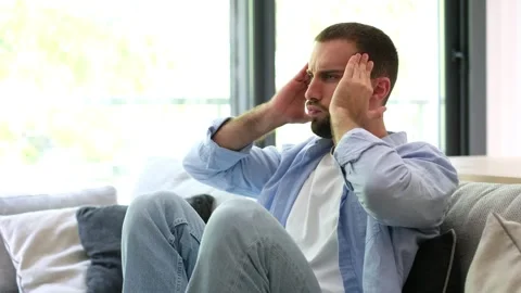 Stressed young man suffering from a headache at home Stock Footage 335588580