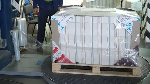 Stretch wrapping machine putting cling wrap around cargo on palettes Stock Footage 74107794