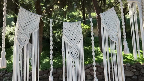 Stretching a garland of white macrame threads in garden Stock Footage 245880115