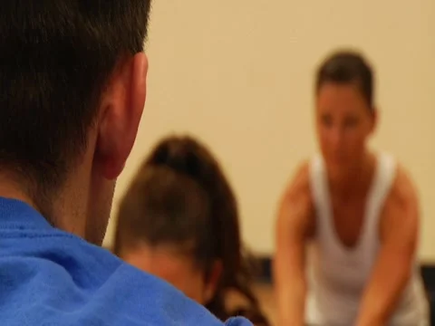 Stretching over-the-shoulder of trainer with rack focus to trainees Stock Footage 7728166