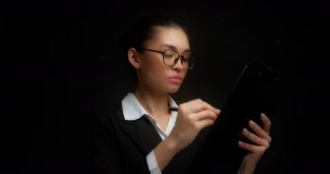 A strict brunette on an isolated black background signs documents. Stock Footage 194775283