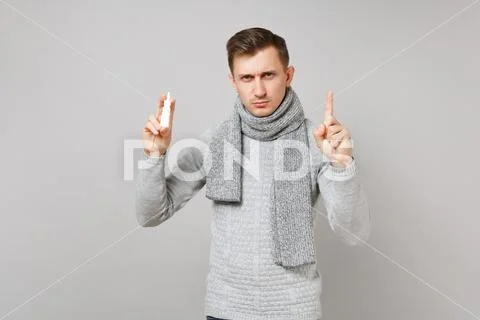 Strict young man in gray sweater, scarf holding nasal drops pointing index Stock Photos