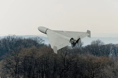 Strike unmanned aircraft performs combat flight above forest landscape. Stock Photos