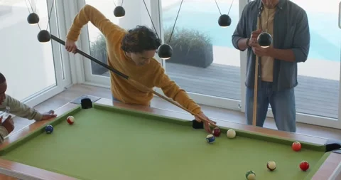 Striking cue ball at home pool table, diverse male friends exchanging advice Stock Footage 335683223