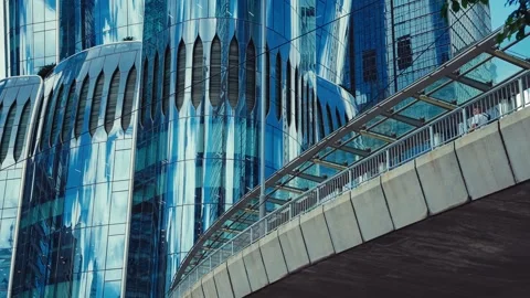 A striking curved pedestrian bridge spanning over a sleek glass-clad skyscraper Stock Footage 338311543