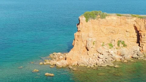 A striking rocky red cliff rises from the clear turquoise waters along the Stock Footage 346692312