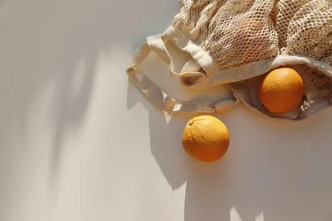 String bag with oranges fruit on beige table background in sunlight. Long Fotos Stock