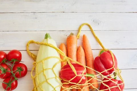 String bag with various fresh vegetables on white textured background. Stock Photos