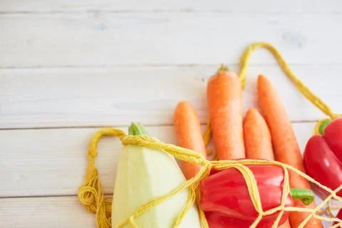 String bag with various fresh vegetables on white textured background. Stock Photos