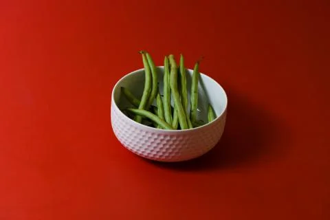 String beans fresh green closeup in cup on isolated red background Stock-Fotos