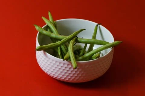 String beans fresh green closeup in cup on isolated red background Stock-Fotos
