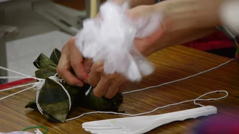 String being hand tied onto rice triangle wrapped in leaf placed on table Stock Footage 195293739