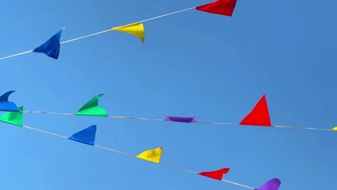 A string of colorful triangular flags hangs across a clear blue sky, waving in t Stock Footage 331671682
