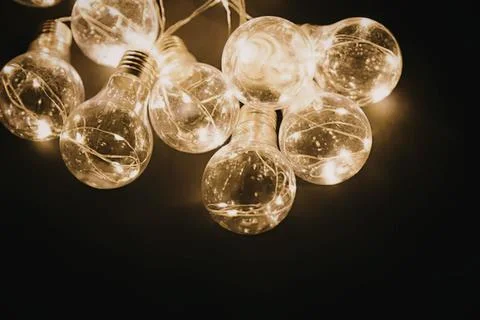 String of glowing light bulbs hanging in dark background Stock Photos