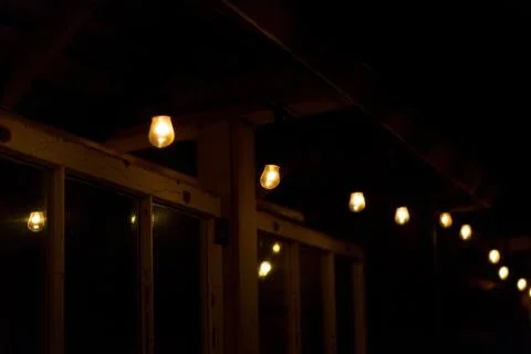 String Of Illuminated Light Bulbs hanging from the house roof at night Stock Photos