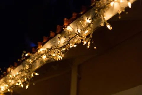 String Of Illuminated Light Bulbs hanging from the house roof at night Stock Photos