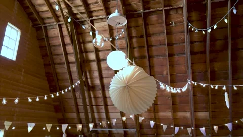 String lights and paper lantern wedding decorations hanging in barn Stock Footage 220456338