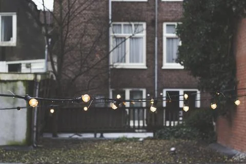 String lights in the back of an urban yard with a brick house and fences in.. Stock Photos