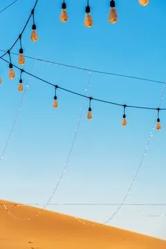 String lights hang against a clear blue sky, with a sandy desert dune Stock Photos