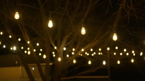 String lights hanging between trees on a terrace at night Video stock 306330816