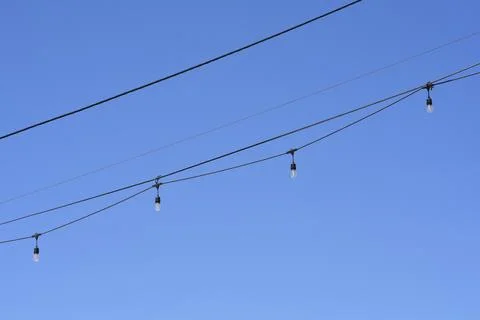 String lights hanging on cables against blue sky Stock Photos