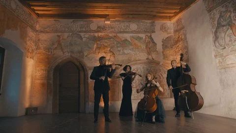 String quartet plays music in a medieval room as the camera pans slightly Stock Footage 92563885