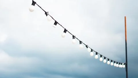 A string of round white light bulbs hanging against a cloudy blue sky Stock Photos
